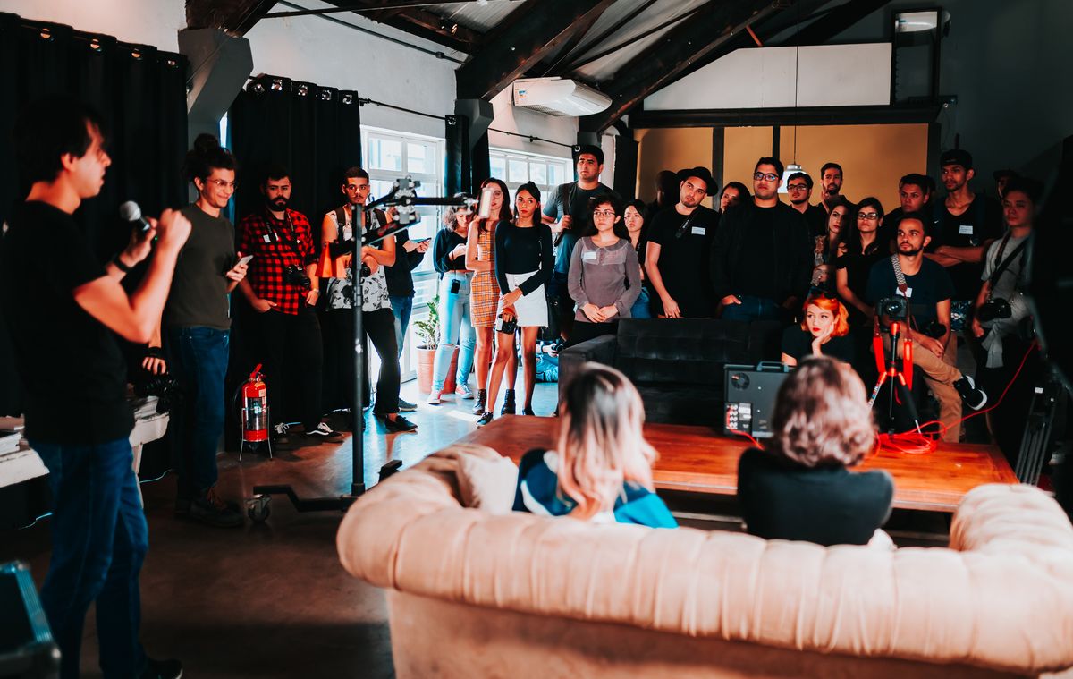 Asistentes reunidos en un evento, con dos personas conversando en un sillón al frente