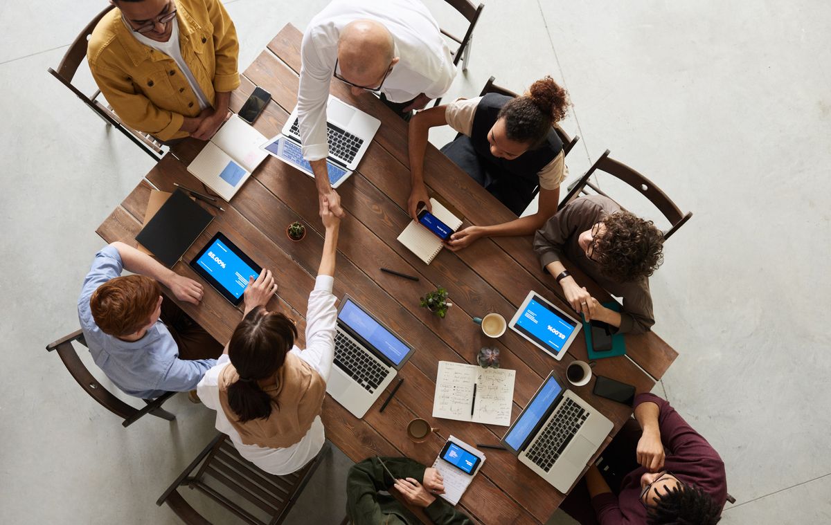 Equipo reunido alrededor de una mesa de trabajo con laptops y tabletas, visto desde arriba