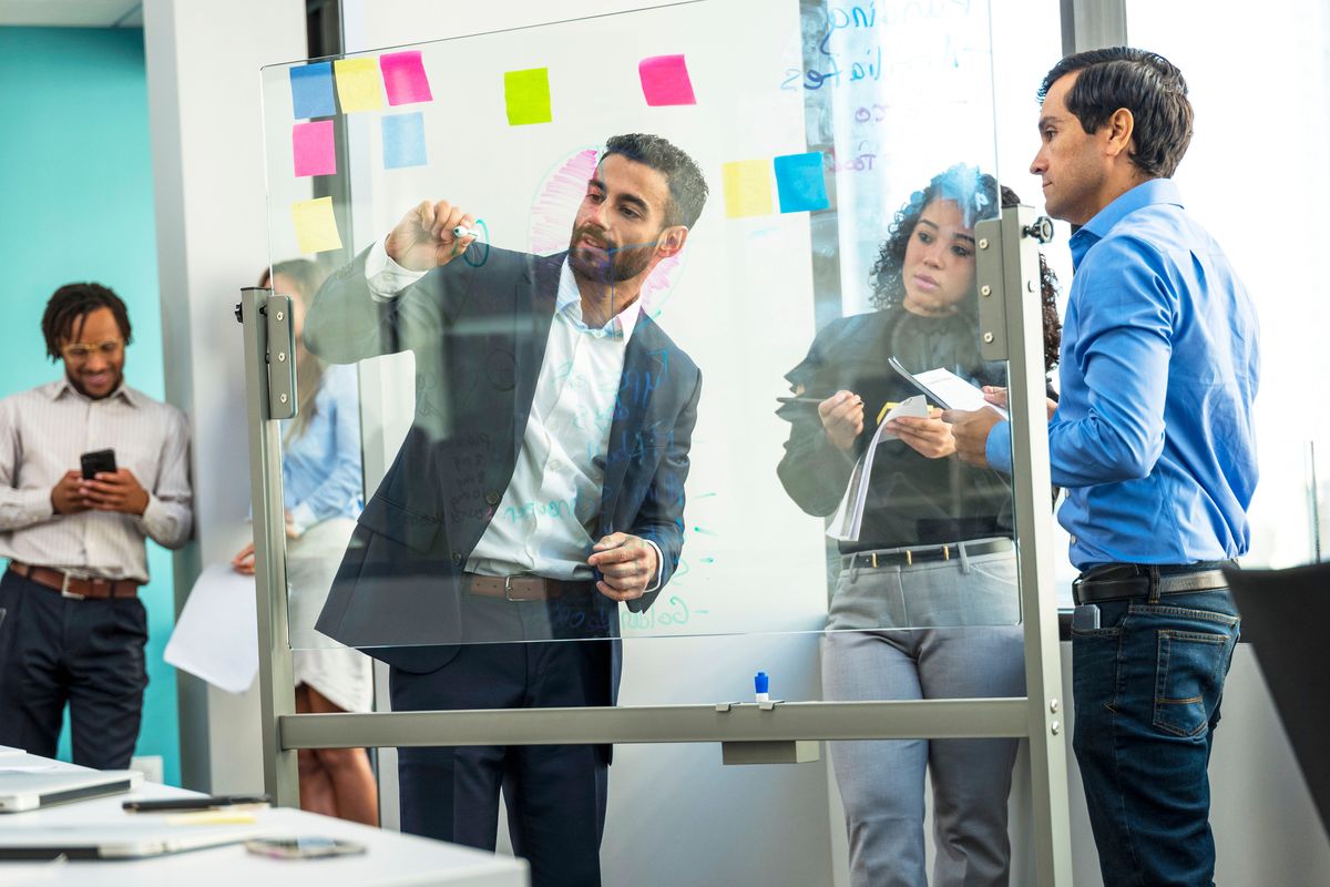 Equipo trabajando con notas adhesivas sobre un pizarrón de cristal en un taller